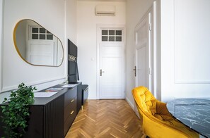A hallway with a mirrored wall, a desk with papers, a potted plant, a yellow chair, and a white door. - Romantic City Light Loft with Premium Comforts & Central Location – 513 (Budapest)