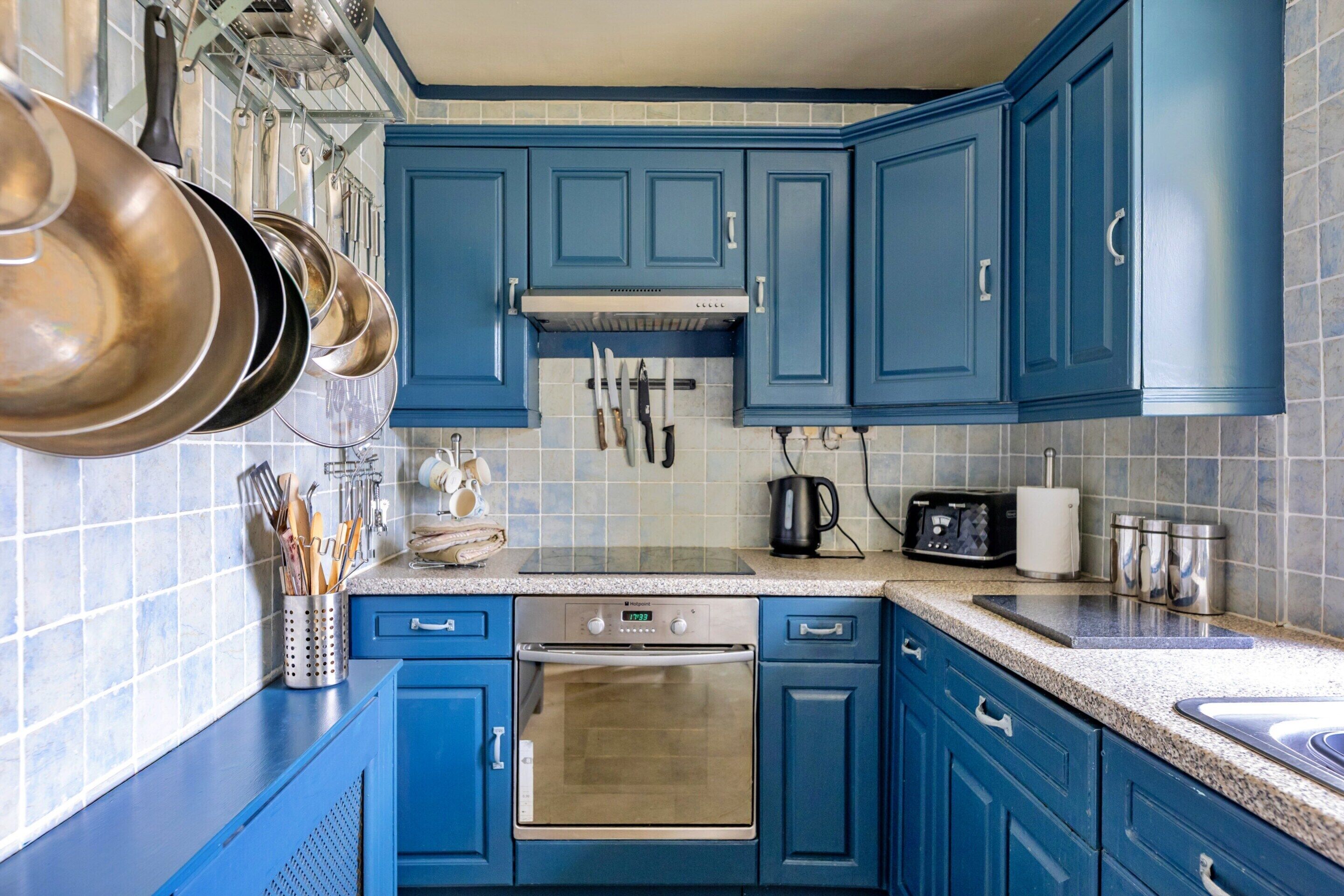 Uma cozinha com armários azuis, eletrodomésticos de aço inoxidável e diversos utensílios pendurados na parede.