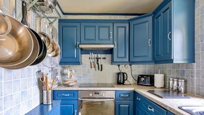 A kitchen with blue cabinets, stainless steel appliances, and a variety of utensils hanging on the wall. - Holiday Cottage With Conwy Castle View (Conwy)