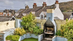 A courtyard with a stone fireplace, surrounded by greenery and a white wall. - Holiday Cottage With Conwy Castle View (Conwy)