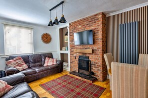 Ein Wohnzimmer mit Kamin aus Backstein, einem Ledersofa, einem an der Wand befestigten Fernseher und einem gemusterten Teppich.