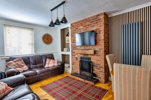 A living room with a brick fireplace, a leather sofa, a television mounted on the wall, and a patterned rug.