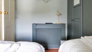 A bedroom with two beds, a wall-mounted TV, a small table with a decorative item, and a door with a golden handle. - Holiday Cottage With Conwy Castle View (Conwy)