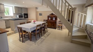 Une cuisine spacieuse équipée d’appareils électroménagers modernes, un coin repas avec une table pour quatre personnes et un escalier menant à l’étage supérieur.