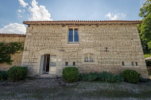 Un bâtiment en pierre avec un toit recouvert de tuiles, une entrée centrale et deux fenêtres.