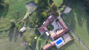 Vue aérienne d’une propriété résidentielle dotée d’une piscine, de plusieurs bâtiments et d’un espace vert environnant.