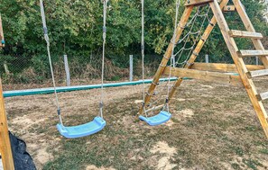 A wooden swing set with two swings and a ladder, surrounded by a chain-link fence and greenery. - Maison Familiale en Campagne (Levis)