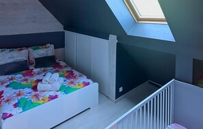 A bedroom with a skylight, a bed with floral bedding, and a white crib. - Maison Familiale en Campagne (Levis)