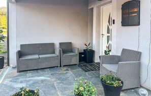 A covered outdoor seating area with two wicker sofas and a single chair, a potted plant, and a door with a decorative panel. - Maison Familiale en Campagne (Levis)