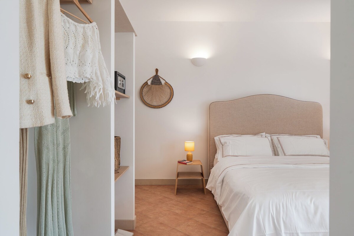 Een slaapkamer met een bed, bedlampje, een wandmand en een plank met decoratieve spullen.