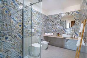Een badkamer met douche, toilet en wastafel, met een betegelde vloer en een houten handdoekrek.