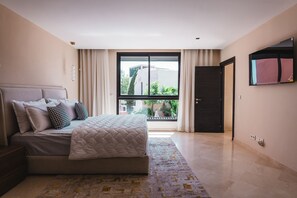 A bedroom with a large bed, a view of greenery outside, and a modern door. - Riad Koutobia – Al Maaden Golf – Marrakech (Marrakech)