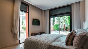 A bedroom with a large bed, a TV on the wall, and a view of a pool and greenery outside. - Riad Koutobia – Al Maaden Golf – Marrakech (Marrakech)