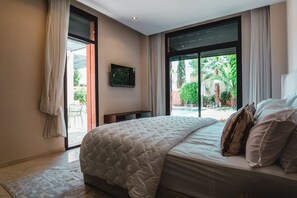 Ein Schlafzimmer mit einem großen Bett, einem Fernseher an der Wand und Blick auf einen Pool und Grünflächen.