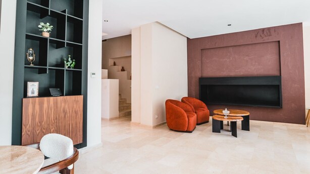 A modern living room with a flat-screen TV, a wooden cabinet, and a seating area with orange chairs. - Riad Koutobia – Al Maaden Golf – Marrakech (Marrakech)