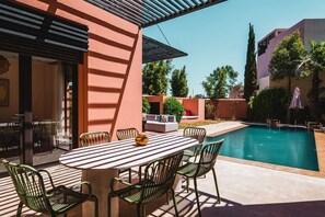 A poolside area with a table and chairs, a covered seating area, and a swimming pool. - Riad Koutobia – Al Maaden Golf – Marrakech (Marrakech)