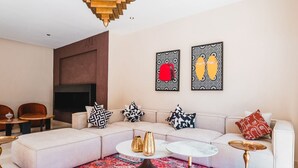 A modern living room with a sectional sofa, a flat-screen TV, and decorative pillows. - Riad Koutobia – Al Maaden Golf – Marrakech (Marrakech)