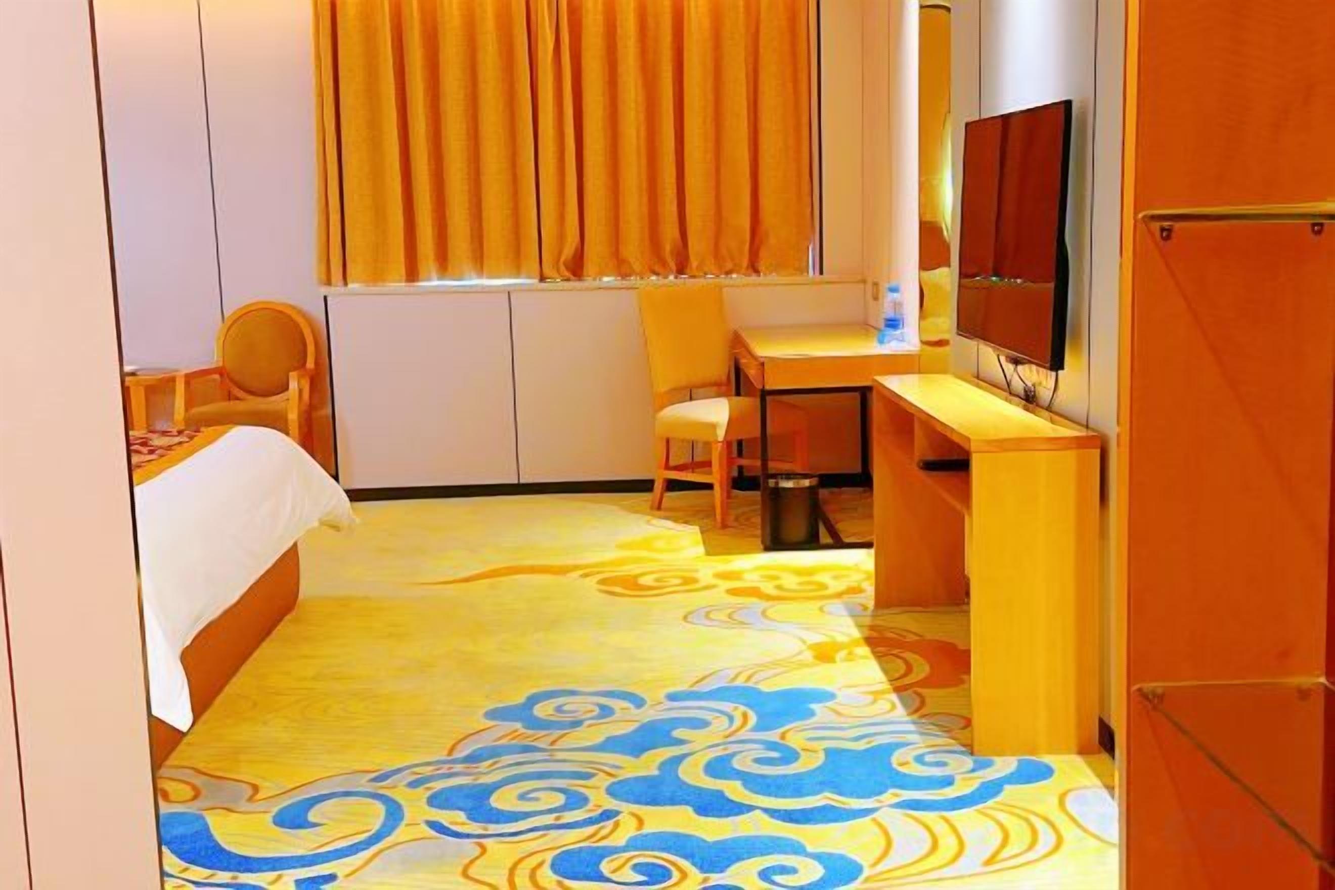 Quarto de hotel com cama, escrivaninha, cadeira, televisão e janela com cortinas.