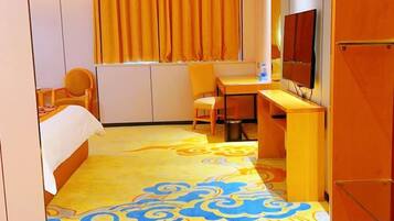 Quarto de hotel com cama, escrivaninha, cadeira, televisão e janela com cortinas.