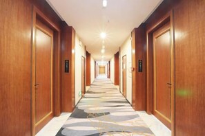 A hotel corridor with wooden doors, a patterned carpet, and a ceiling light. - Dongguan Jinzhenghe Hotel (Dongguan)