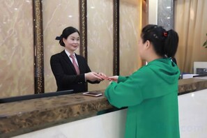 A reception desk with a marble counter and a person in a green jacket handing over a card to a receptionist. - Dongguan Jinzhenghe Hotel (Dongguan)