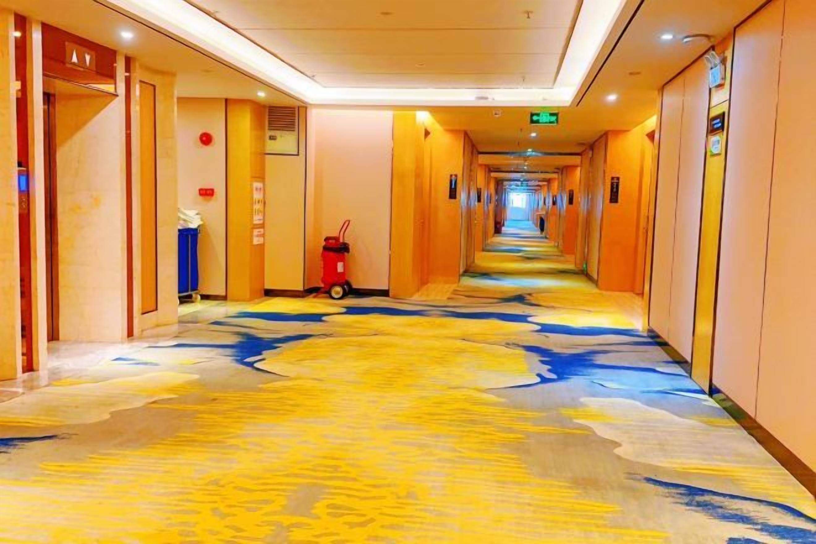 Un pasillo de hotel con alfombra estampada, puertas a ambos lados y un extintor a la izquierda.