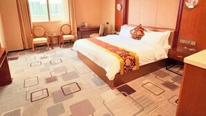 A hotel room with a large bed, a desk, two chairs, a small table, and a view of the city. - Dongguan Jinzhenghe Hotel (Dongguan)