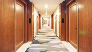 A hotel corridor with wooden doors, a patterned carpet, and a ceiling light. - Dongguan Jinzhenghe Hotel (Dongguan)