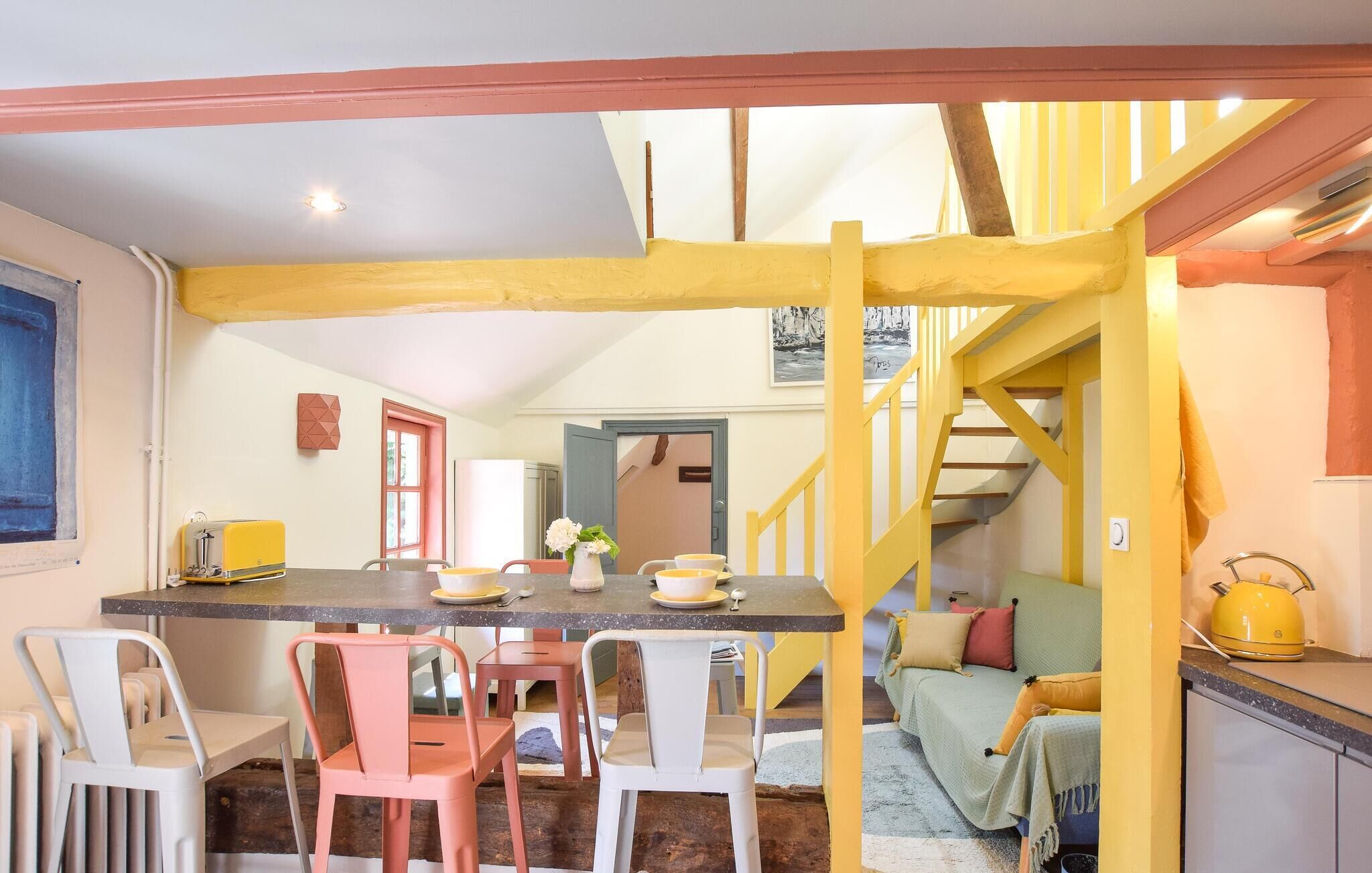 A dining area with a table set for four, chairs, a yellow staircase, and a kitchen area with a kettle.