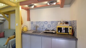 Una cocina con un microondas amarillo, una tetera y un lavamanos. Hay una escalera con barandillas amarillas que conduce a un nivel superior.