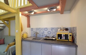 Una cocina con un microondas amarillo, una tetera y un lavamanos. Hay una escalera con barandillas amarillas que conduce a un nivel superior.