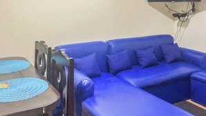 A living room with a blue sofa, a flat-screen TV mounted on the wall, and a small table with blue placemats. - Seawind Condominium (Davao City)