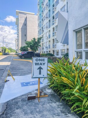 Uma área de estacionamento com placa de 'SENTIDO ÚNICO', vaga para deficientes e um edifício com vários andares e varandas.