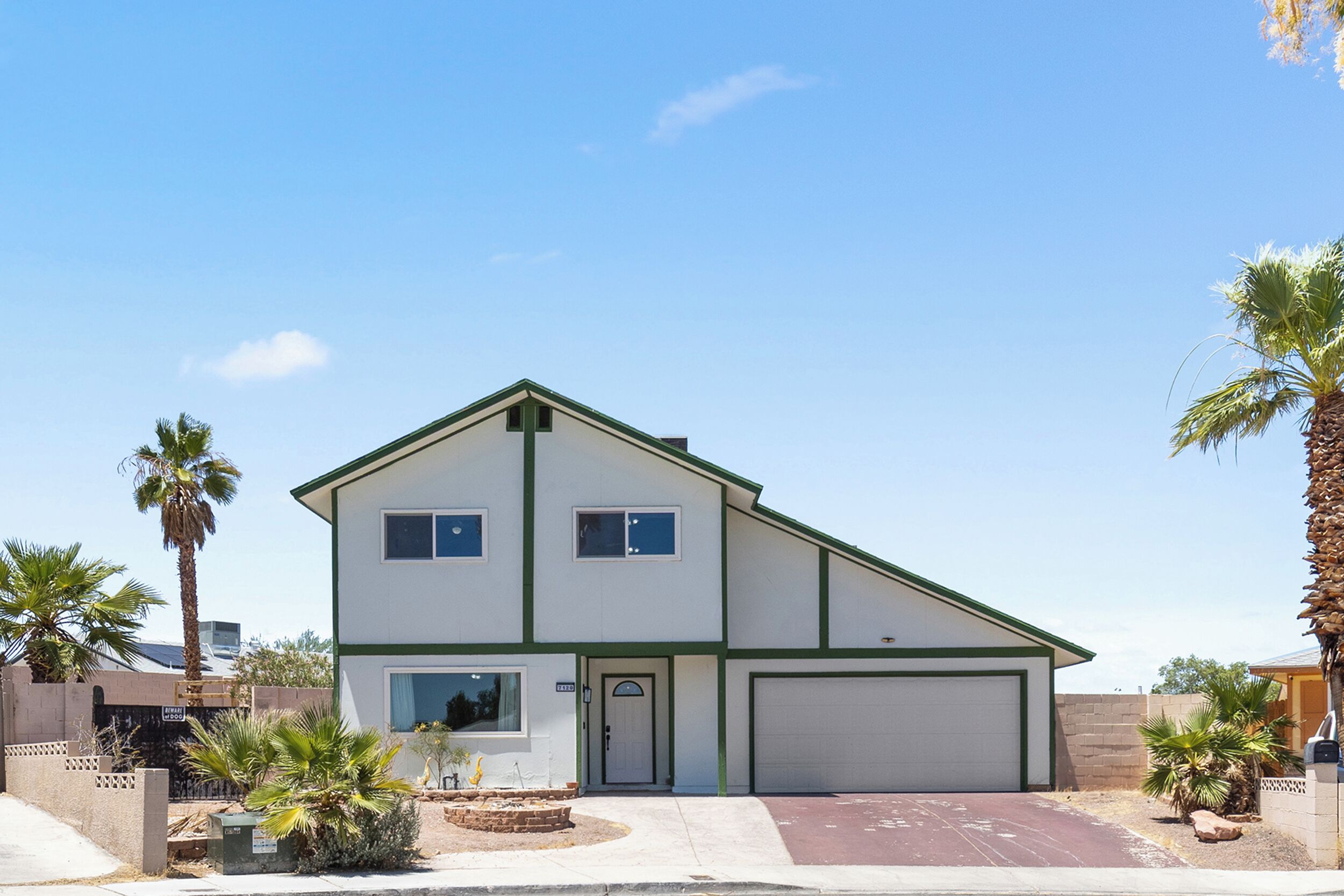 A two-story house with a garage, surrounded by palm trees and a clear sky.