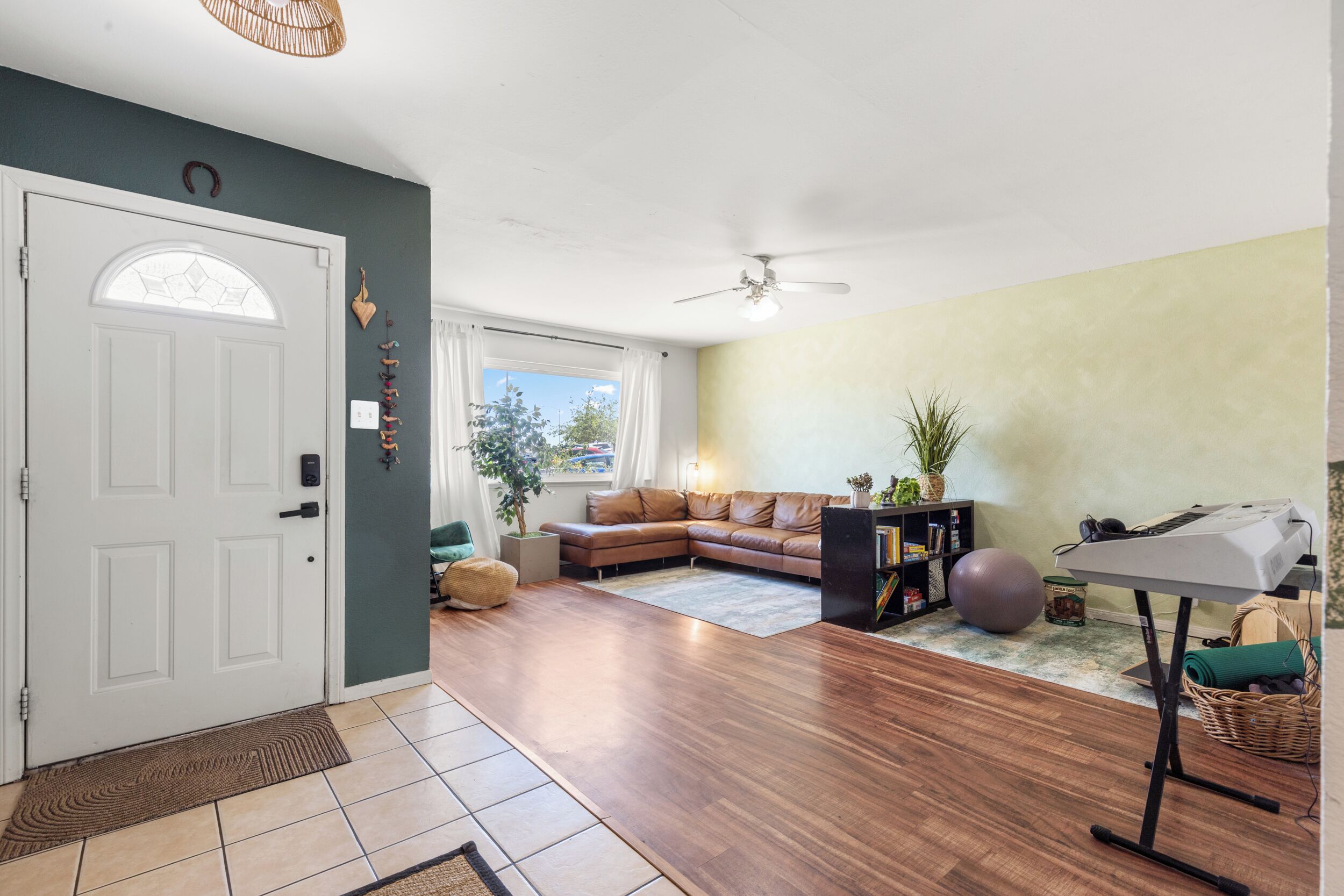 Un salon avec un canapé en cuir marron, une petite table avec un clavier, un ventilateur de plafond et une porte avec une fenêtre.