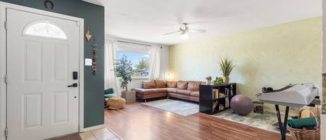 A living room with a brown leather sofa, a small table with a keyboard, a ceiling fan, and a door with a window.