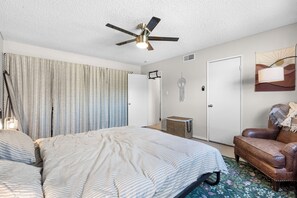 A bedroom with a bed, a ceiling fan, a door, and a wall-mounted artwork. - Fun-Filled, Pet-Friendly 4BR Home w/ Private Halfpipe, Small Pool & Hot Tube! (Las Vegas)