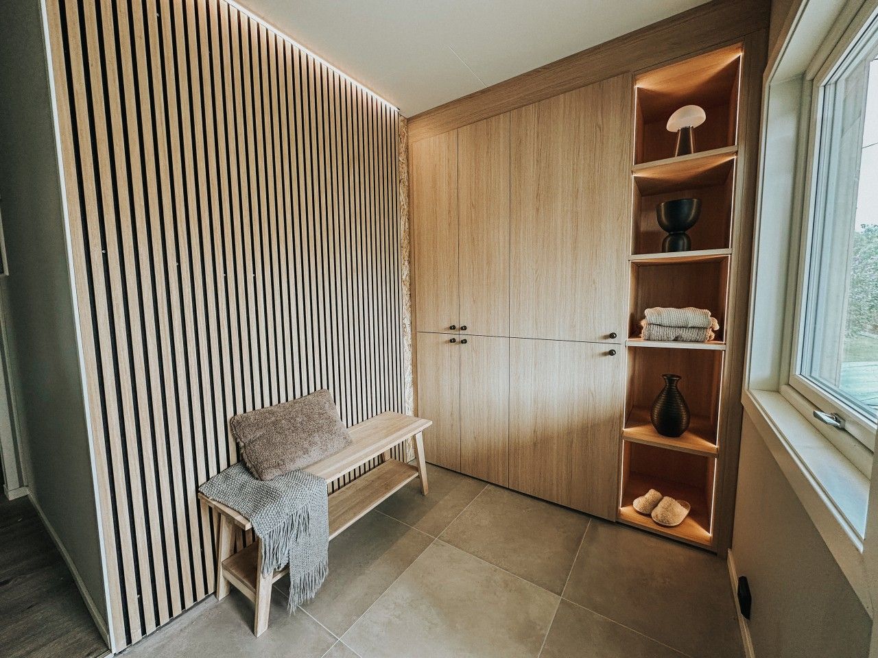 A room with a bench, a wooden wardrobe, and a shelf with items.
