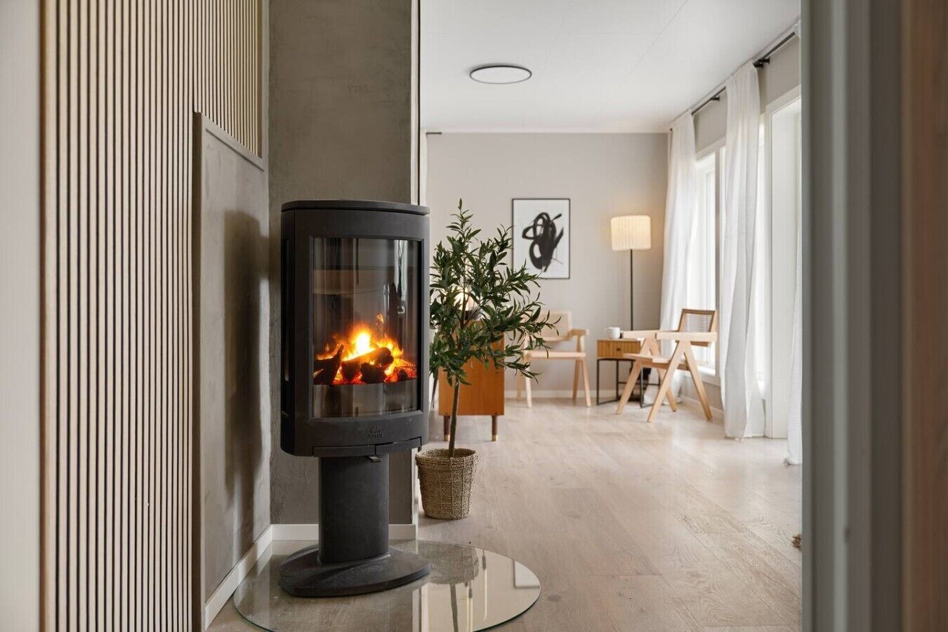 Un salon moderne avec un poêle à bois, une plante en pot et un coin repas comprenant une table et des chaises.