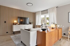 A modern living room with a flat-screen TV, a wooden cabinet, a white sofa, and a dining table with candles. - Exclusive South Tromsøya home peaceful & central (Tromsø)