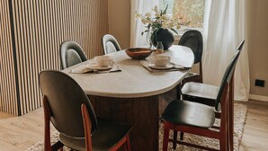 A dining area with a round table, six chairs, a vase with flowers, and a hanging light fixture. - Sydpol Designer Home Northern Lights View (Tromsø)