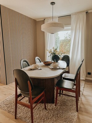 A dining area with a round table, six chairs, a vase with flowers, and a hanging light fixture. - Sydpol Designer Home Northern Lights View (Tromsø)