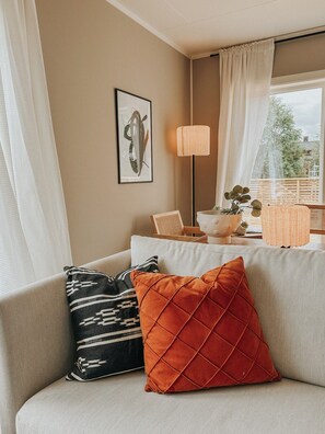 A living room with a sofa, cushions, a floor lamp, a framed artwork, and a view through a window. - Sydpol Designer Home Northern Lights View (Tromsø)