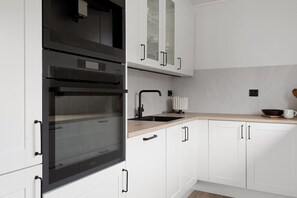 A modern kitchen with white cabinetry, a black oven, and a wooden countertop. - Exclusive South Tromsøya home peaceful & central (Tromsø)