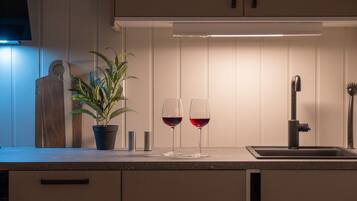 A kitchen with a countertop, two wine glasses, a potted plant, and a sink.