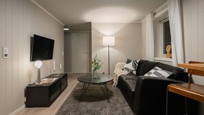 A modern living room with a flat-screen TV, a round coffee table, a sofa, and a lamp. - Sydpol Designer Home Deluxe Apartment (Tromsø)