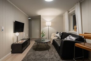 A modern living room with a flat-screen TV, a round coffee table, a sofa, and a lamp. - Sydpol Designer Home Deluxe Apartment (Tromsø)