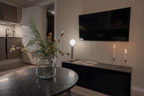 A modern living room with a round table, a vase with dried flowers, a flat-screen TV mounted on the wall, and two candles on a side table. - Sydpol Designer Home Deluxe Apartment (Tromsø)