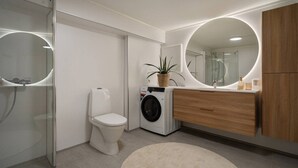 Une salle de bain moderne avec une douche à parois de verre, des toilettes, un lave-linge et un meuble-lavabo en bois avec un miroir.