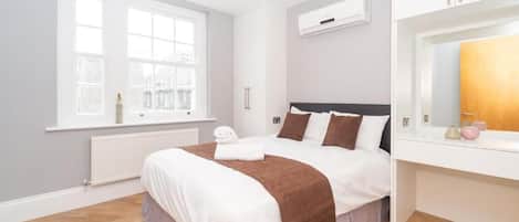 A hotel room with a bed, a window, a radiator, and a white cabinet.